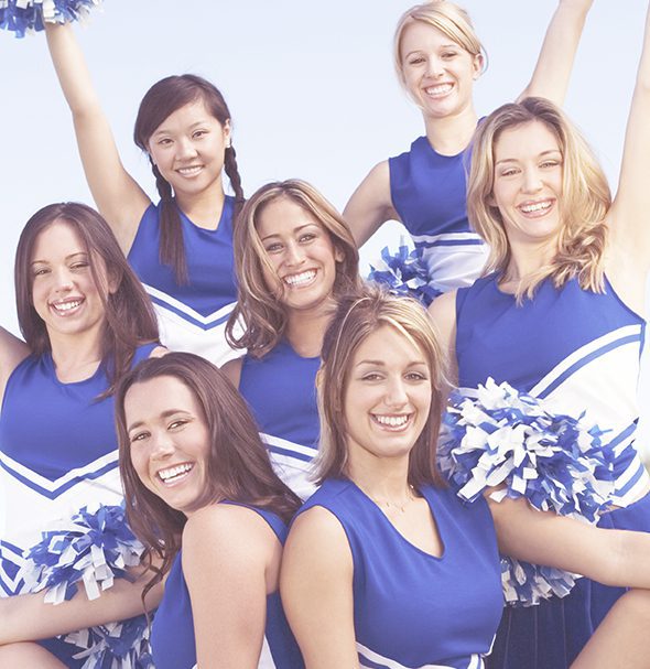 Teenage cheerleaders smiling wearing blue and white uniforms and holding pompoms.