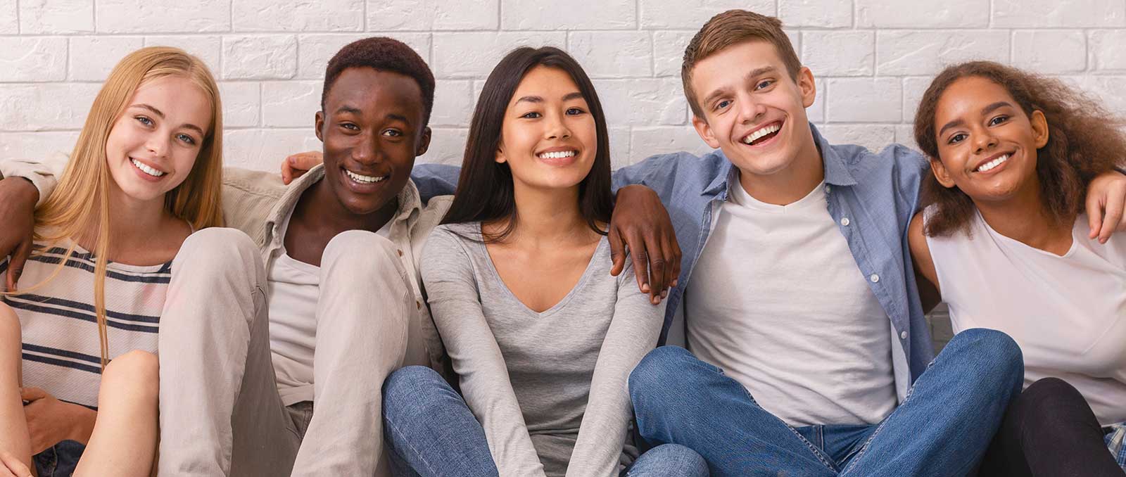 Diverse group of teens with arms around each other smiling.