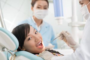 Young girl laying in dentists chair while the dentist holds a small mirror up to her mouth